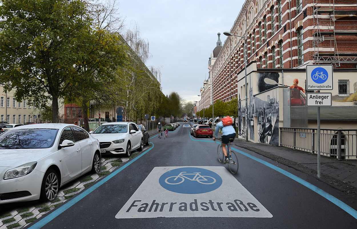 Blick in die visualisierte Fahrradstraße in der Nonnenstraße in Leipzig Plagwitz mit blau markiertem Radweg und weißer Aufschrift "Fahrradstraße" auf der Straße, rechts ein großes Backsteingebäude und mehrere parkende Autos links.