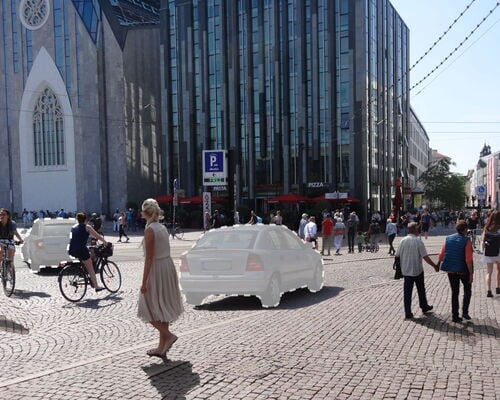 Menschen und Radfahrer auf gepflastertem Platz vor moderner Glasfassade und historischer Kirche bei klarem Himmel