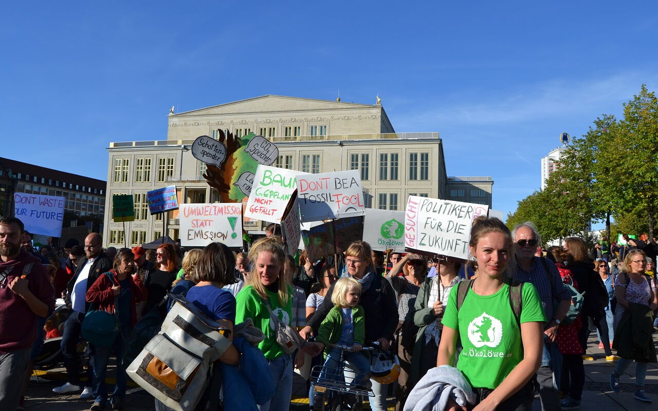 Menschenmenge bei einer Klimademonstration vor einem großen historischen Gebäude, der Leipziger Oper, mit verschiedenen Protestschildern