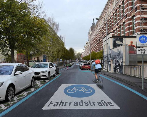 Blick in die visualisierte Fahrradstraße in der Nonnenstraße in Leipzig Plagwitz mit blau markiertem Radweg und weißer Aufschrift "Fahrradstraße" auf der Straße, rechts ein großes Backsteingebäude und mehrere parkende Autos links.