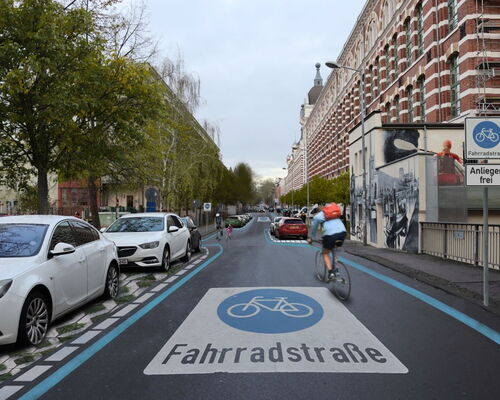 Blick in die visualisierte Fahrradstraße in der Nonnenstraße in Leipzig Plagwitz mit blau markiertem Radweg und weißer Aufschrift "Fahrradstraße" auf der Straße, rechts ein großes Backsteingebäude und mehrere parkende Autos links.