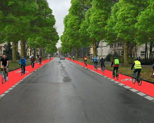 Eine breite, asphaltierte Straße wird von hohen, belaubten Bäumen gesäumt. Auf beiden Seiten der Fahrbahn verlaufen auffällig rote Radwege mit weißen Fahrradsymbolen.