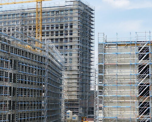 Mehrere hohe Gebäude in unterschiedlichem Bauzustand umgeben von Gerüsten und einem gelben Baukran