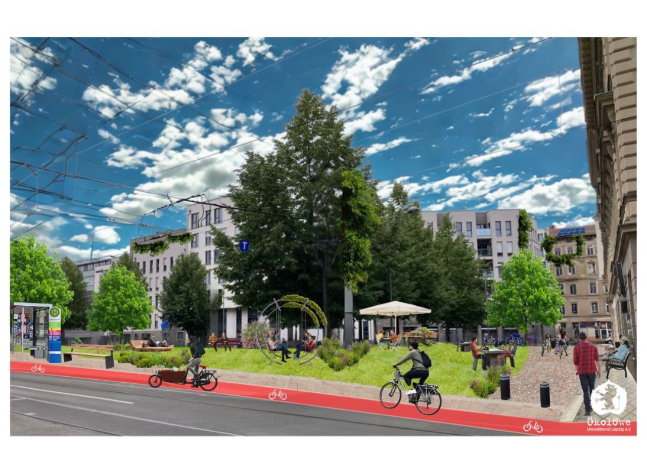 grüner Stadtplatz mit Bäumen, Wiese und Sitzgelegenheiten. Im Vordergrund eine Straßenbahnhaltestelle mit rotem Radweg davor mit Radfahrer:innen.