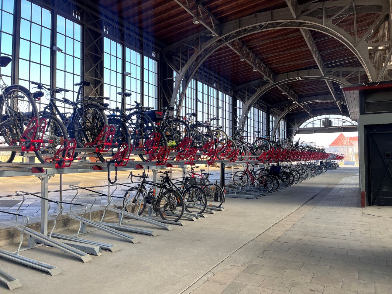 Überdachte Fahrradgarage mit zweistöckigen Fahrradständern und mehreren abgestellten Fahrrädern unter einem hohen, gewölbten Dach mit großen Fenstern.